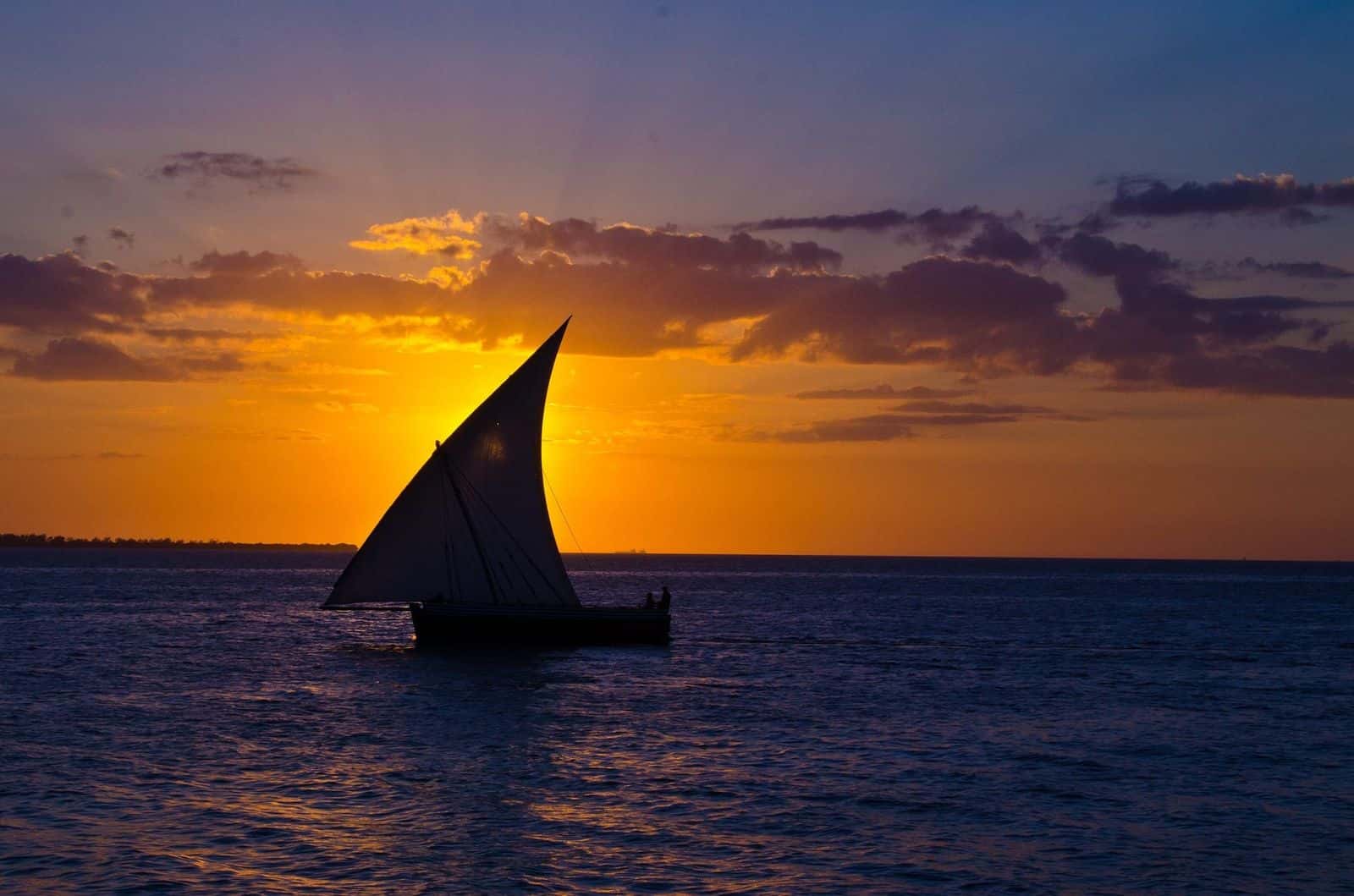 A traditional dhow sailing against an orange sunset