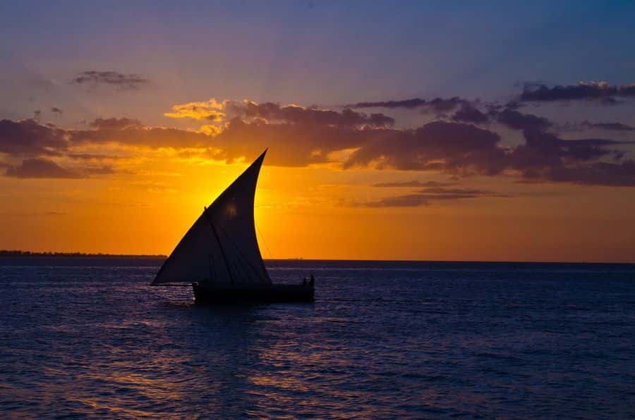 A traditional dhow sailing against an orange sunset