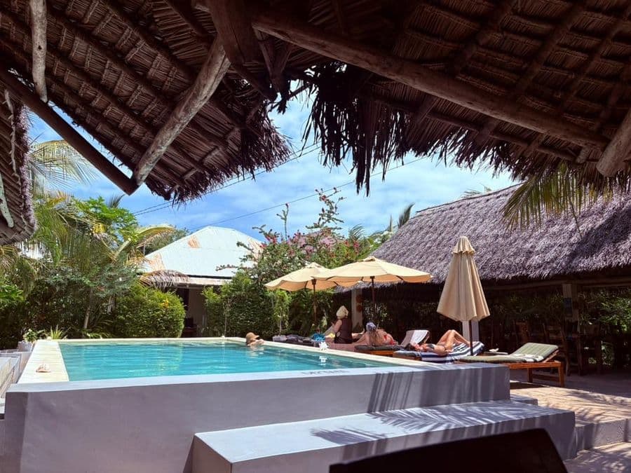 Guests relaxing on sun loungers beside the pool under thatched roofs