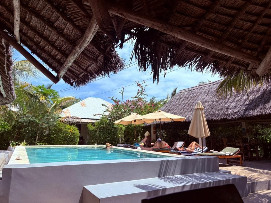 Guests relaxing on sun loungers beside the pool under thatched roofs