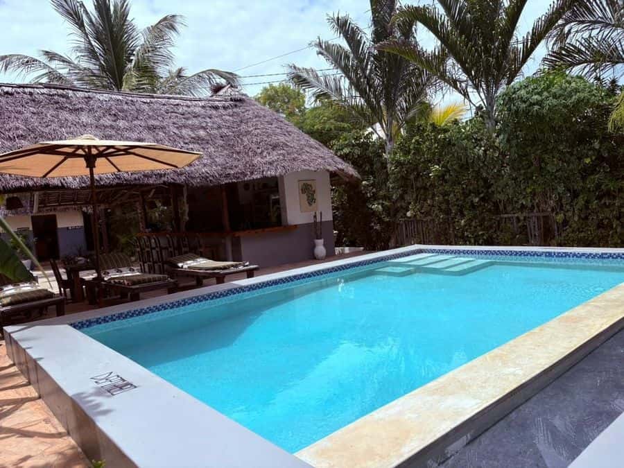 Turquoise swimming pool with an umbrella and thatched building behind